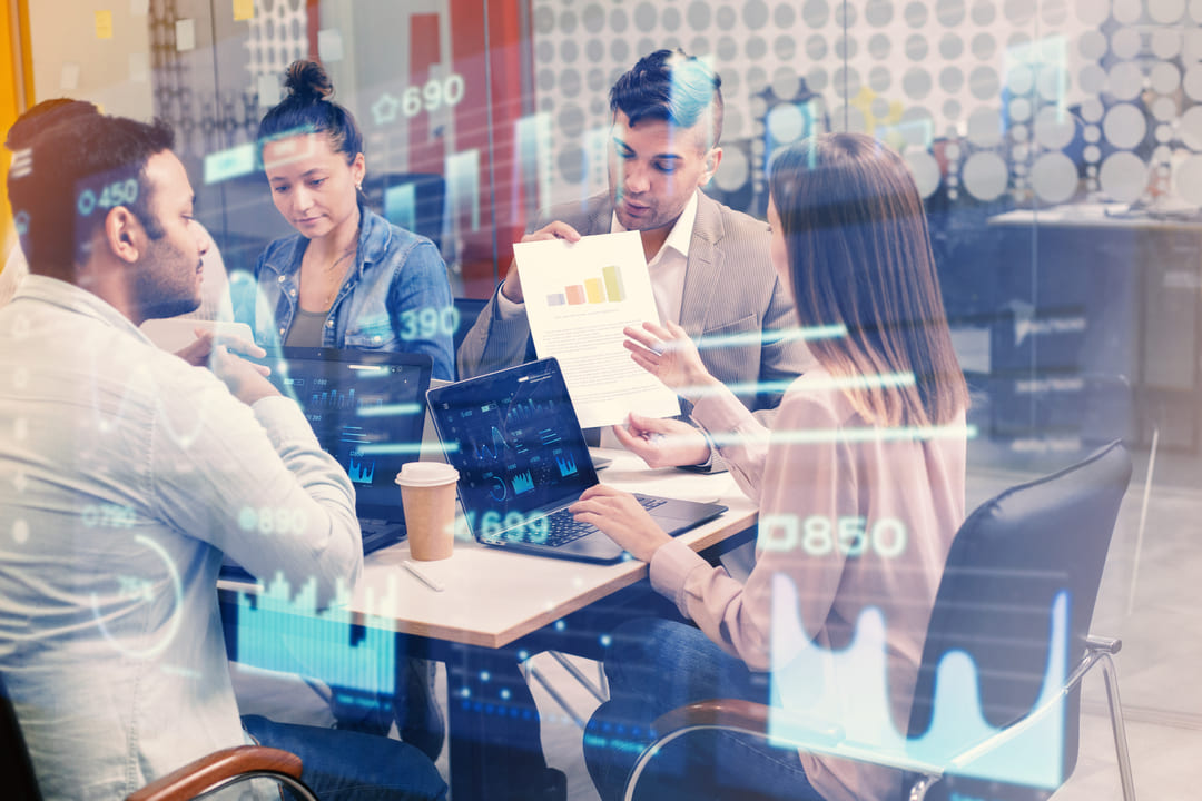 Equipe de negócios discutindo análise de dados e gráficos financeiros em uma reunião, com projeções holográficas de estatísticas e números digitais sobrepostos à imagem.