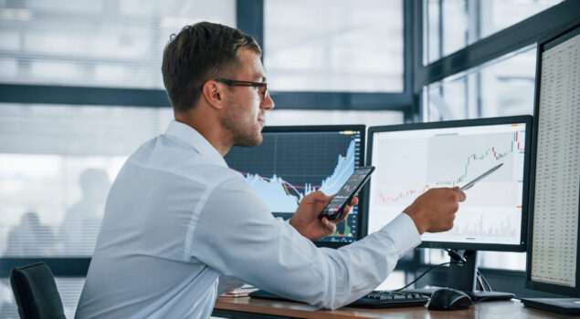 Profissional analisando gráficos financeiros em múltiplas telas, com celular na mão, representando automação contábil e análise de dados em tempo real.