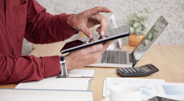 Transformação digital na contabilidade: contador usando tablet em escritório com laptop, calculadora e relatórios financeiros.