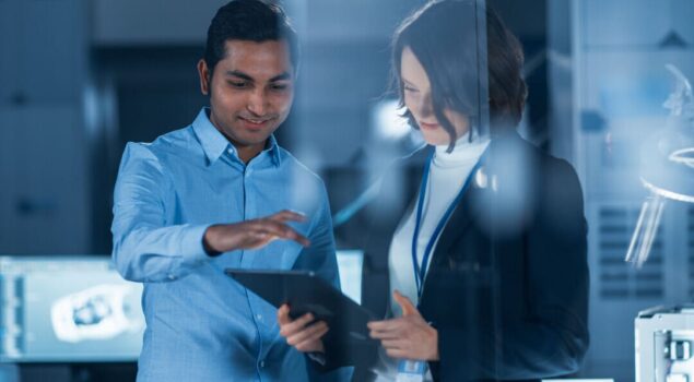 Dois profissionais de tecnologia analisando informações em um tablet em um ambiente de laboratório ou escritório moderno.