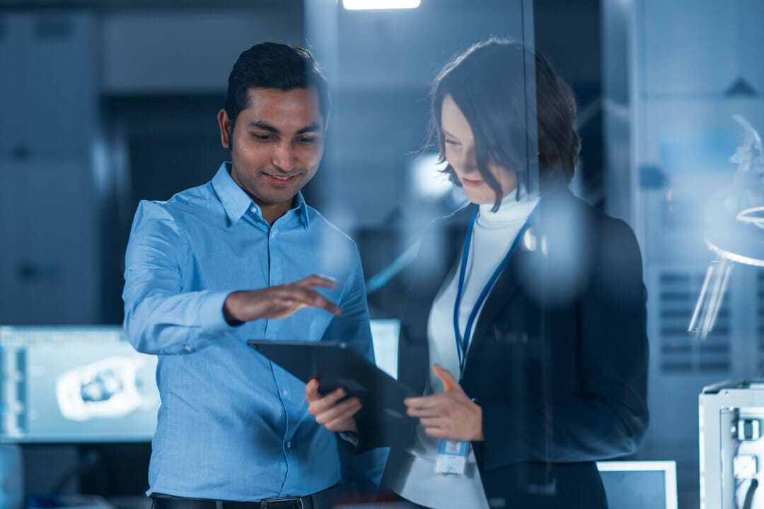 Dois profissionais de tecnologia analisando informações em um tablet em um ambiente de laboratório ou escritório moderno.