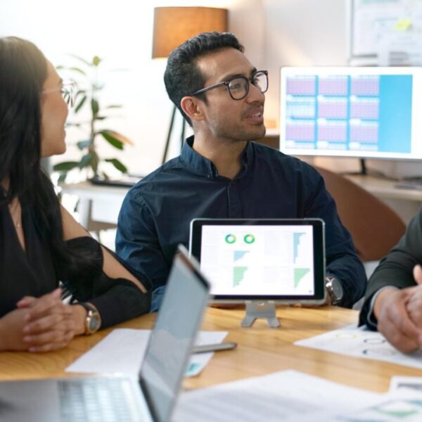 Equipe em reunião analisando gráficos e indicadores exibidos em um tablet e computadores.