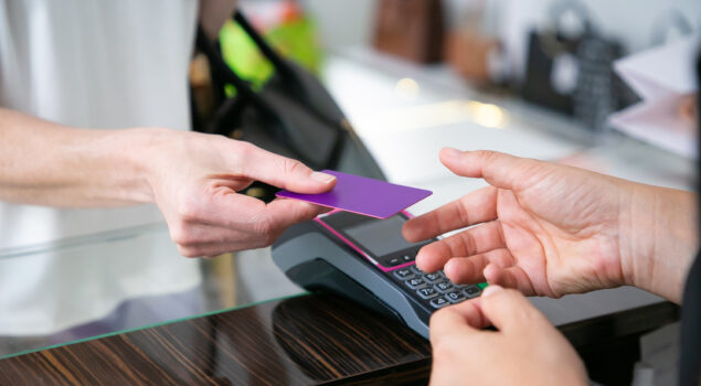 Mão de um cliente entregando um cartão a um atendente para pagamento em uma maquininha, representando o processo de conciliação de cartões em transações financeiras.
